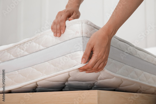 Woman putting soft white mattress on bed indoors, closeup