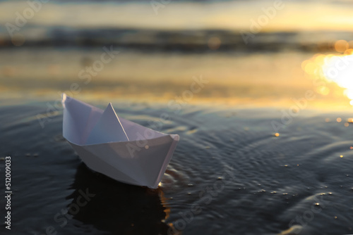 White paper boat in shallow water of sea at sunset, space for text