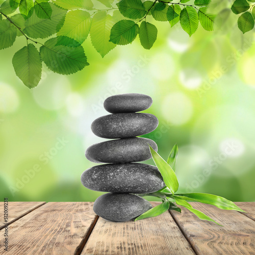Stacked stones and bamboo stems on wooden table under green leaves against blurred background. Zen concept