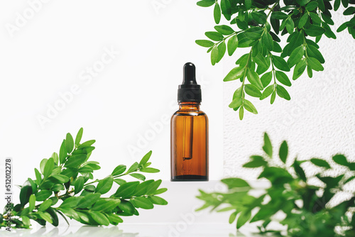 Fototapeta Naklejka Na Ścianę i Meble -  Natural medicine or aroma oil or beauty essence concept mockup vial with dropper on glass stand with green plant and white background. Face and body spa serum care concept banner