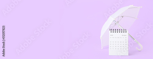 Flip paper calendar and umbrella on lilac background with space for text