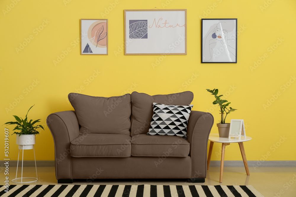 Interior of stylish living room with brown sofa and table near yellow wall Interior of stylish living room with brown sofa and table near yellow wall