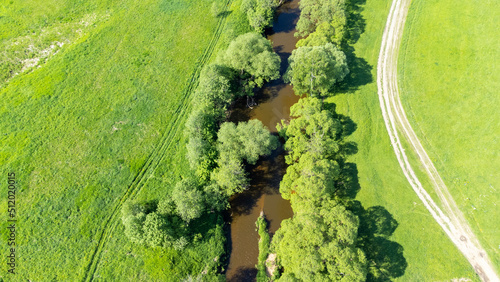 a bird's-eye view of a small river, which is located on a green floodplain meadow. a winding little river with trees on the shore, surrounded by green fields of meadows on a sunny summer day