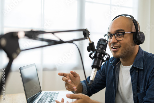 Content creator asia man host streaming his a podcast on laptop with headphones and condenser microphone interview guest conversation at home broadcast studio. Male blogger recording voice over radio