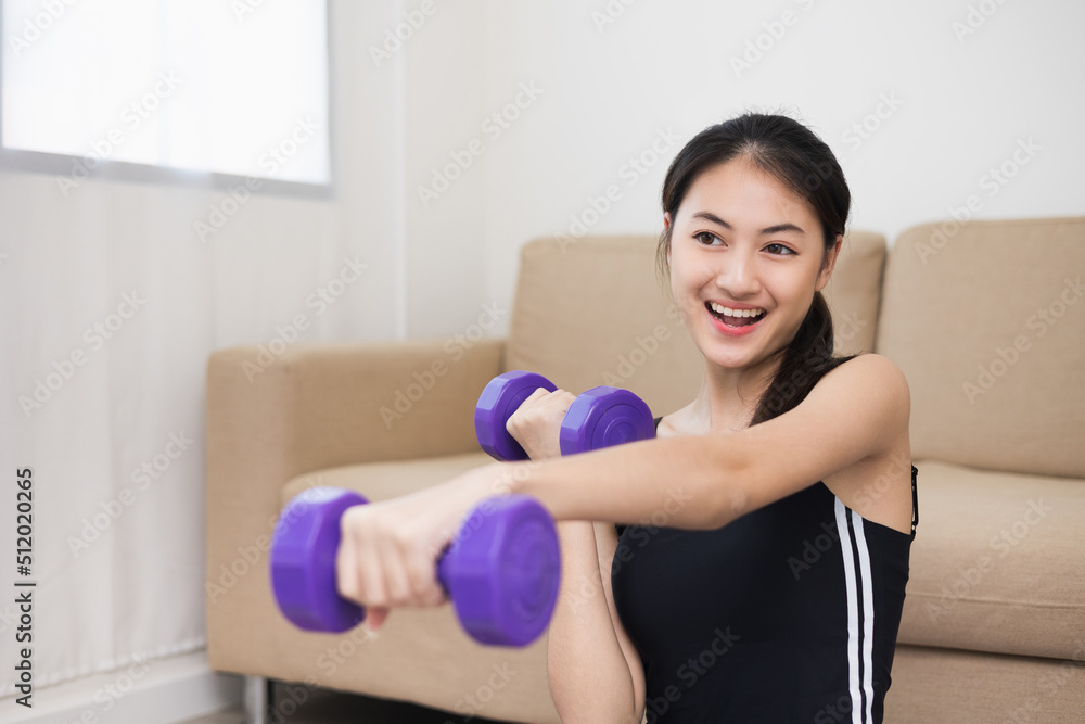 Attractive asian young fitness woman lifting dumbbell weights workout at home in living room. Fresh feeling female training and exercise wearing sport wear fit body.