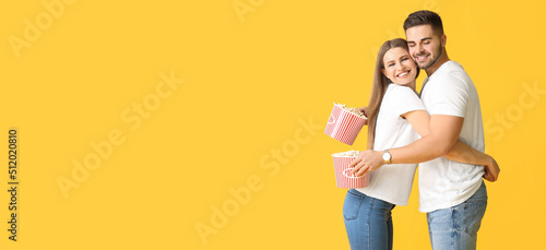 Happy young couple with popcorn on yellow background with space for text © Pixel-Shot