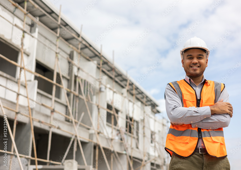 Confident engineer handsome man standing arms crossed at modern home building construction. Architect with white safety helmet at construction site.