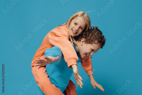 two cute, joyful children in multi-colored sweaters stand on a blue background, a boy rolls a happy girl on his back. The theme of children's friendship and relationships