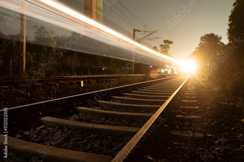 Light trail of the express train in the railway station at the night. High speed passenger train on railroad track in motion at night. Blurred commuter train.