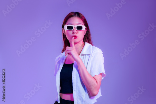 asian woman in black tank top and white shirt wearing sunglasses posing ove isolated purple background.