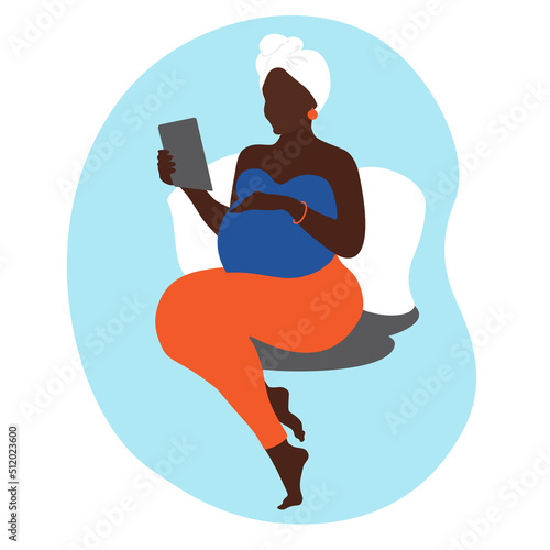 African American pregnant woman communicates via video call on a tablet laptop. Prenatal Consultations online. Pregnancy woman siting on the bed, hand rests on stomach.