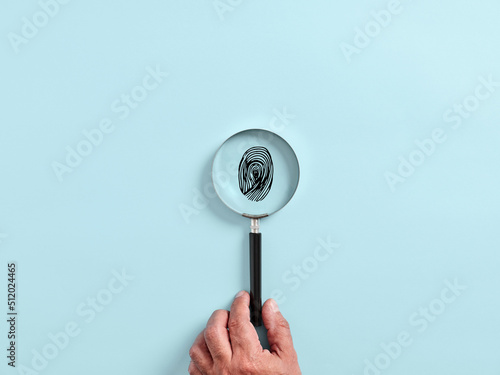 Male hand holds a magnifying glass or magnifier focusing on a fingerprint. Forensic identification photo