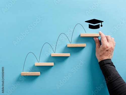Male hand arranges a wooden block ladder with academic cap symbol. Graduation achievement and education goals. photo
