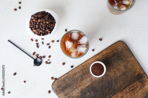 Glass of cold brew with milk and scattered coffee beans on white table © Pixel-Shot
