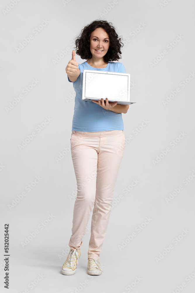 Young pregnant woman with laptop showing thumb-up on light background Young pregnant woman with laptop showing thumb-up on light background