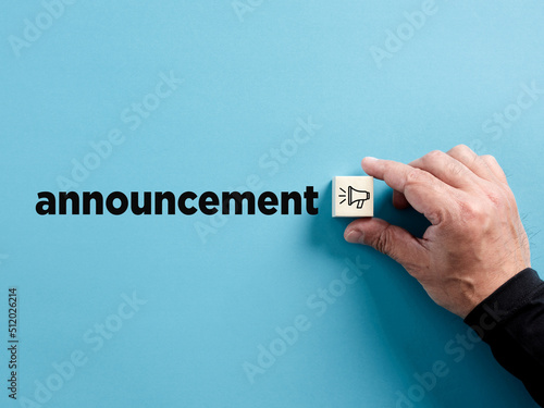 Male hand puts the wooden cube with megaphone symbol next to the word announcement. Important announcement