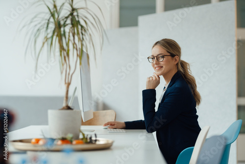 Smiling businesswoman sitting with hand on chin at desk photo