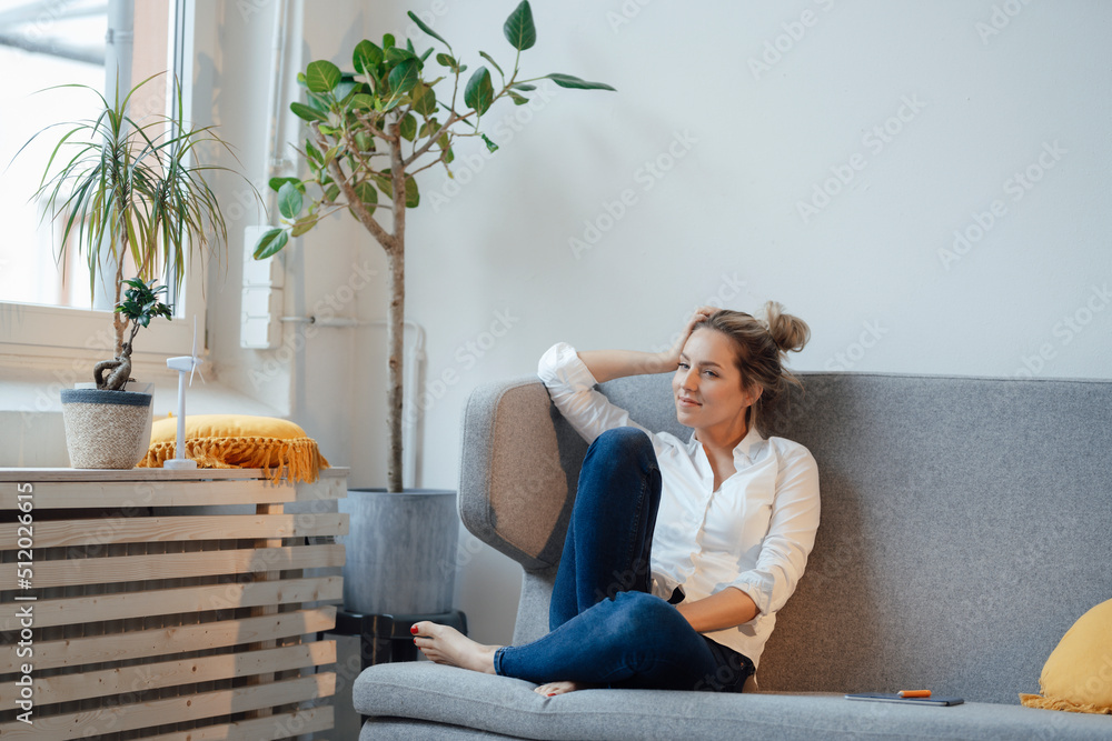 Smiling businesswoman sitting with hand in hair on sofa at office Smiling businesswoman sitting with hand in hair on sofa at office