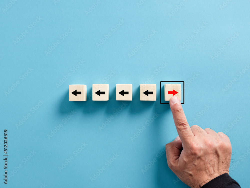 Fototapeta premium Male hand chooses the arrow button facing the opposite direction than the others on wooden cubes.