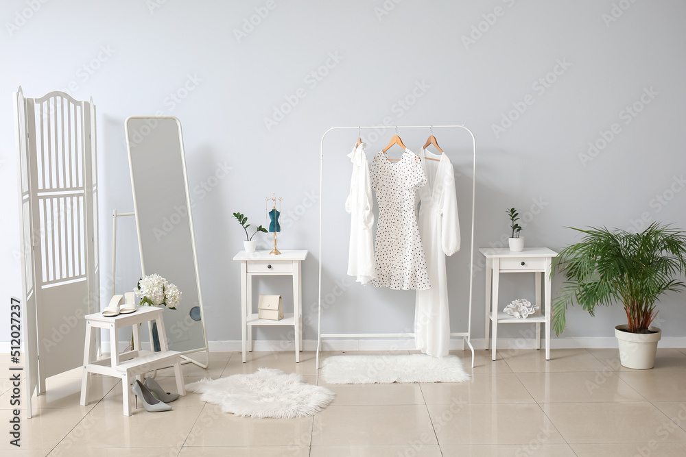 Rack with stylish female clothes, tables and mirror near light wall Rack with stylish female clothes, tables and mirror near light wall