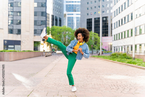 Happy woman with Afro hairstyle kicking on footpath photo