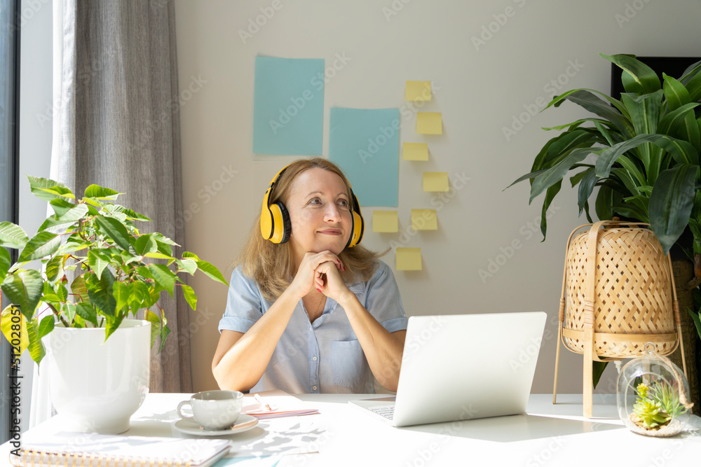 © Westend61 - Thoughtful smiling freelancer listening music through wireless headphones sitting with laptop at desk in home office