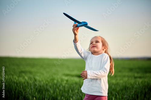 Playful girl flying airplane toy on field at sunset photo