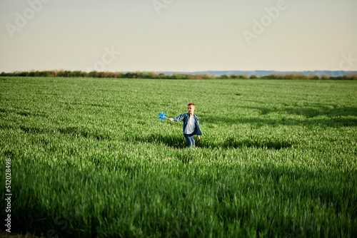 Playful boy with pinwheel toy walking in grassy field photo