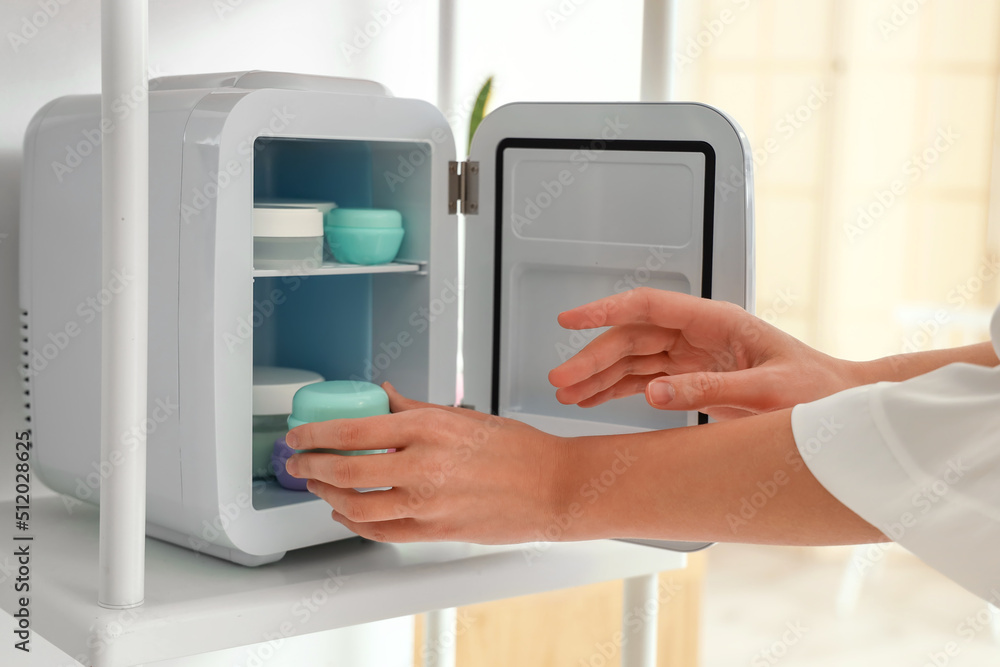 Young woman taking cream from small refrigerator for cosmetic products, closeup Young woman taking cream from small refrigerator for cosmetic products, closeup