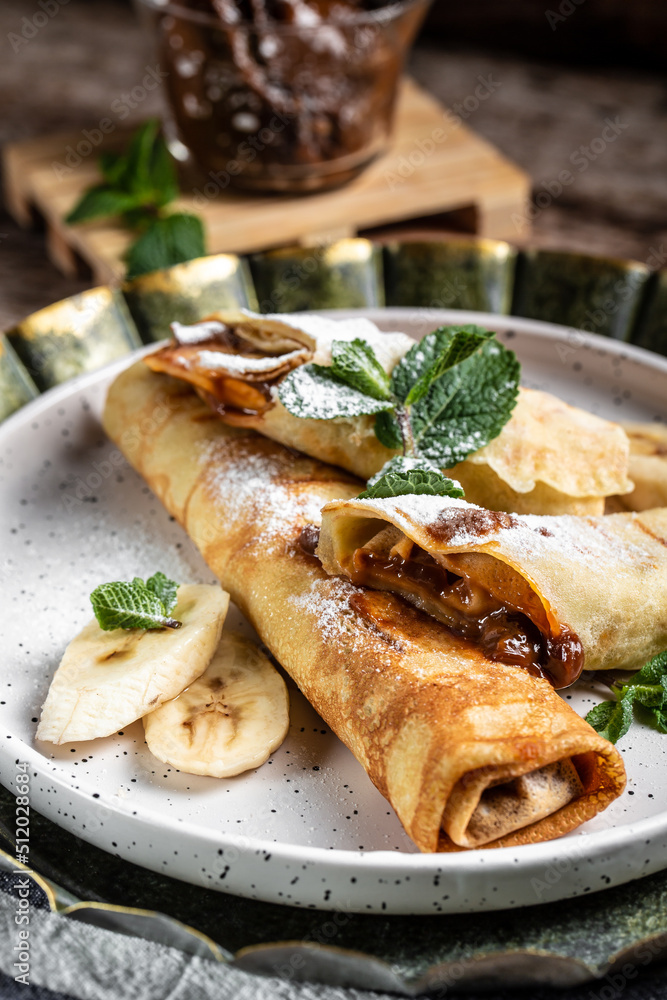 Crepes stuffed with chocolate spread and banana on white plate. Thin pancakes, blini. Delicious breakfast or snack. Food recipe background. Close up Crepes stuffed with chocolate spread and banana on white plate. Thin pancakes, blini. Delicious breakfast or snack. Food recipe background. Close up
