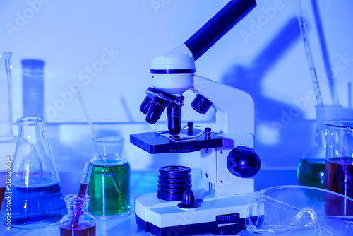 Modern microscope and laboratory glassware on blue background