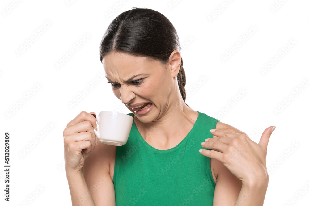 Dissatisfied frowning young woman with a cup of hot drink on a white background Dissatisfied frowning young woman with a cup of hot drink on a white background