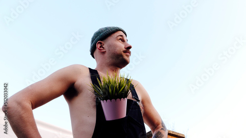 Man wearing knit hat standing with plant in bib overalls photo