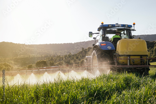 Young farmer spraying fertilizer through sprayer on tractor on field photo