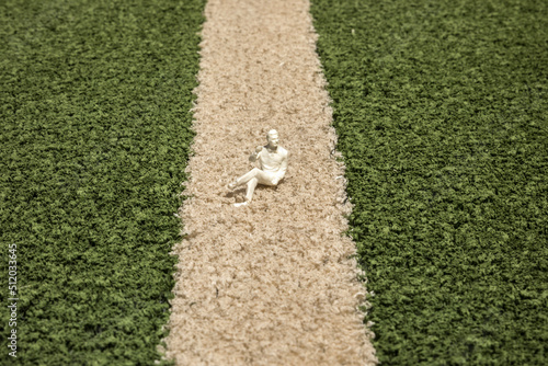 Small figurine lying on artificial grass of soccer field photo