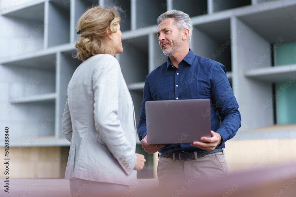 Businessman holding laptop discussing with businesswoman Businessman holding laptop discussing with businesswoman