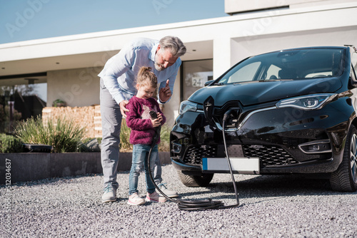 Wallpaper Mural Man talking to daughter holding electric plug in front of car on sunny day Torontodigital.ca