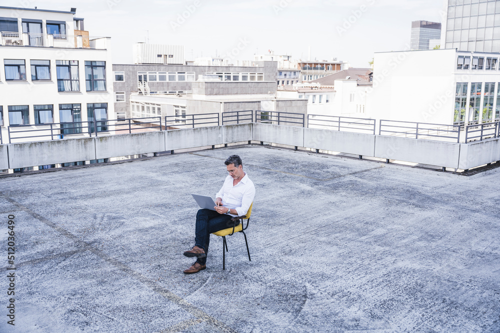 Businessman using laptop sitting on building terrace Businessman using laptop sitting on building terrace