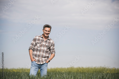 Happy mature man with hands in pockets standing at field on sunny day photo