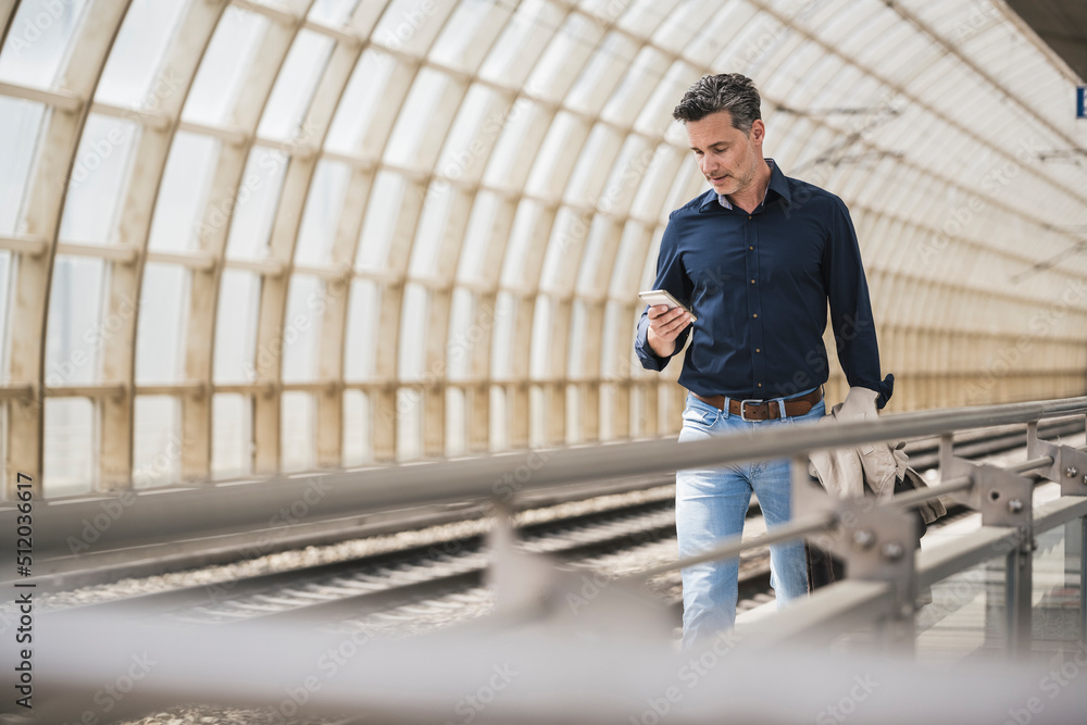 Mature man using smart phone walking at railroad station Mature man using smart phone walking at railroad station