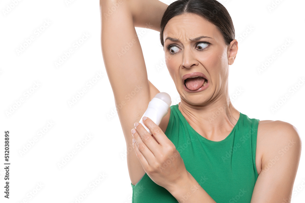 a horrified young woman applies deodorant under her armpits on a white background. a horrified young woman applies deodorant under her armpits on a white background.