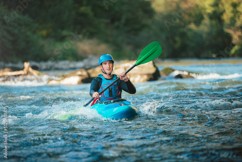 Male recreational athlete paddling carefully over the risky, foamy, and splashy whitewater rapids in his blue kayak