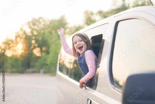 Girl child waves her hand from car window, concept of traveling with children and safety on roads