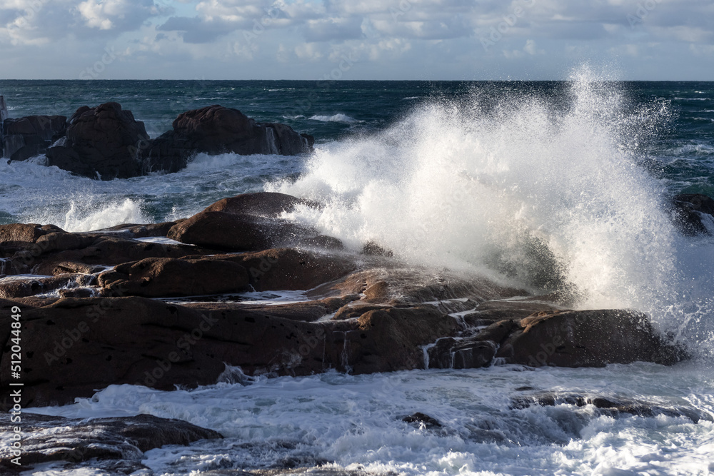 Rough sea and big waves hit rocks creating enormous spray.