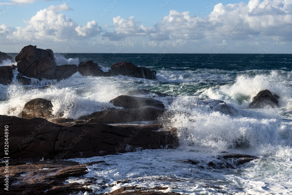 Rough sea and big waves hit rocks under friendly sky.
