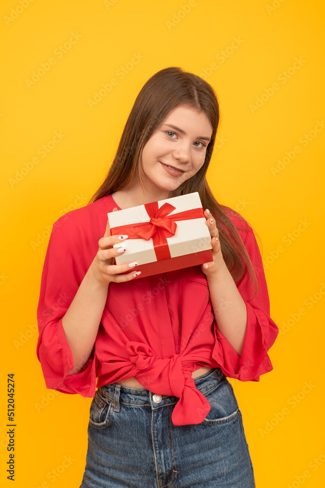 Portrait of young brunette girl in red blouse and jeans with gift box in her hands on bright yellow background. Vertical frame. Portrait of young brunette girl in red blouse and jeans with gift box in her hands on bright yellow background. Vertical frame.