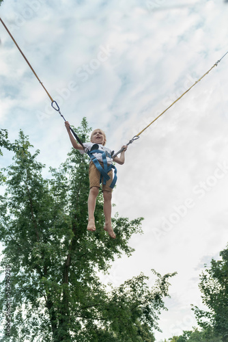 Little boy jumping in an amusement park on the ropes high into sky. Schoolboy has fun in the theme park. Summer vacation