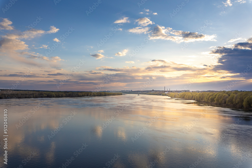 Evening landscape, sunset on the river. Wide river, horizon, clouds are reflected in the water.