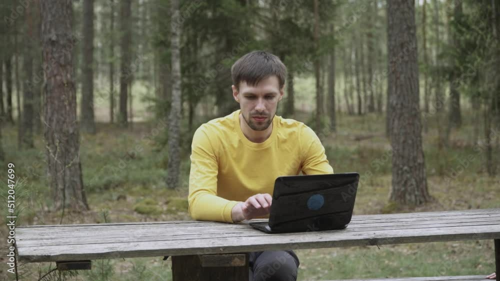 Caucasian man with stubble sits in forest, looks at laptop screen. Guy is surprised, in euphoria rejoices at victory, incredibly happy person. Brunet shakes fists, claps hands, not believing his luck. Caucasian man with stubble sits in forest, looks at laptop screen. Guy is surprised, in euphoria rejoices at victory, incredibly happy person. Brunet shakes fists, claps hands, not believing his luck.