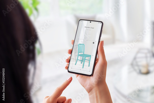 Woman with augmented reality app sets up a wooden chair in living room. Virtual furniture placement with mobile concept